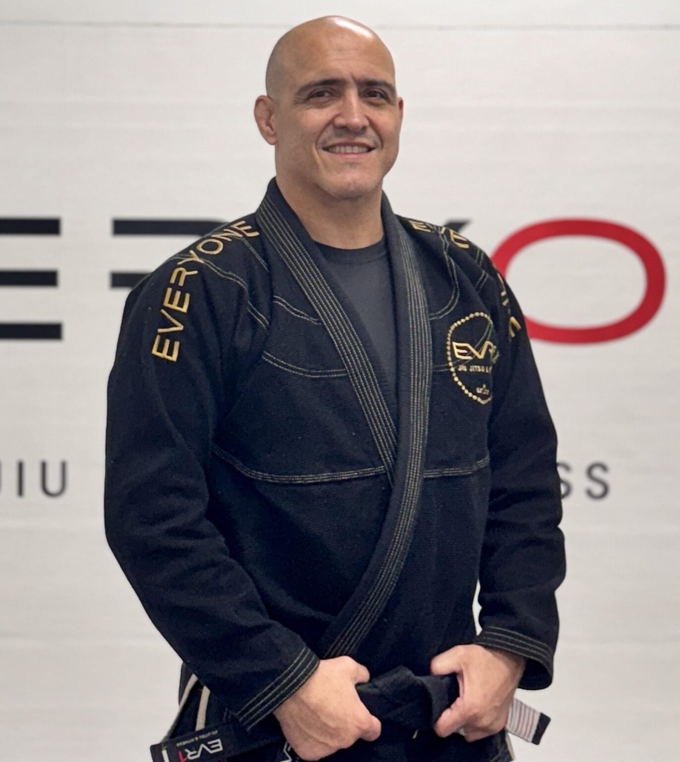 Professor Marcos Escobar in a black gi in front of the academy wall logo