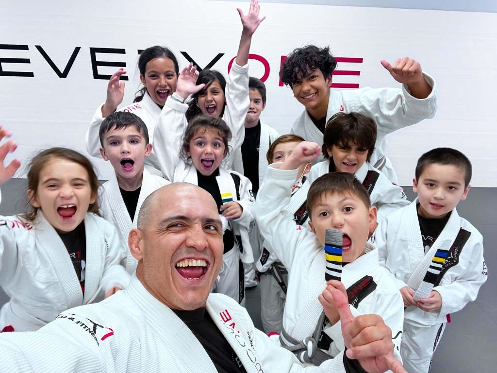 Instructor and a group of kids in gis smiling together after a jiu-jitsu class